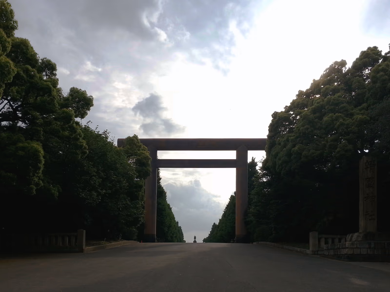 A photograph of a torii gate in a serene landscape with trees on both sides of a road leading to the gate.