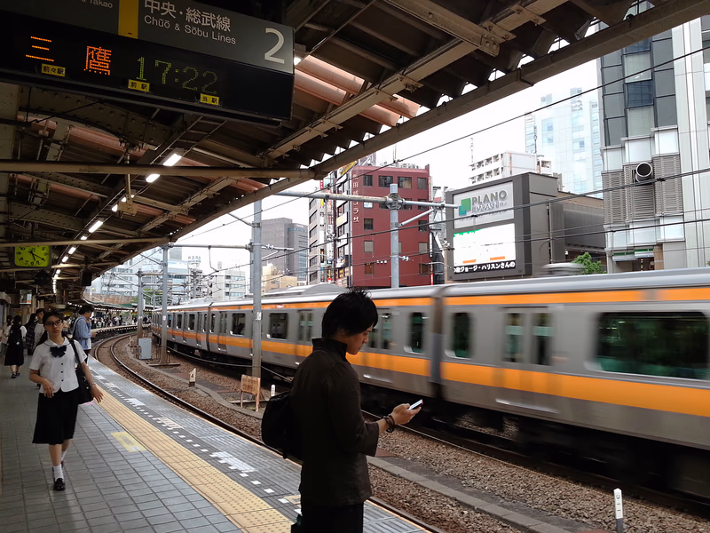 A bustling train station in Tokyo, Japan, with a train passing by and people waiting for their ride.
