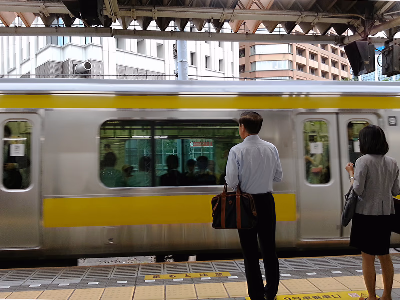 A man and a woman standing on a train platform, with a train passing by.