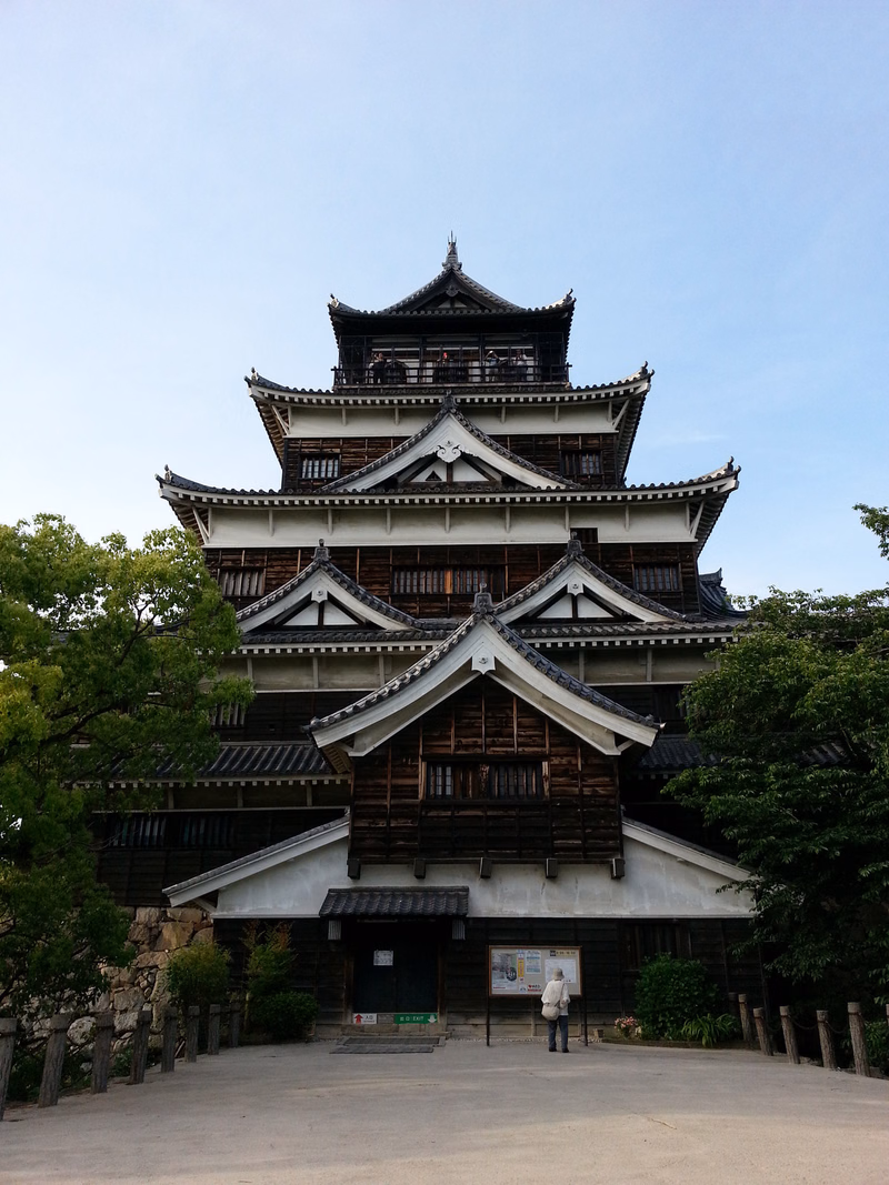 A large, traditional Japanese castle with multiple tiered roofs stands under a clear blue sky.