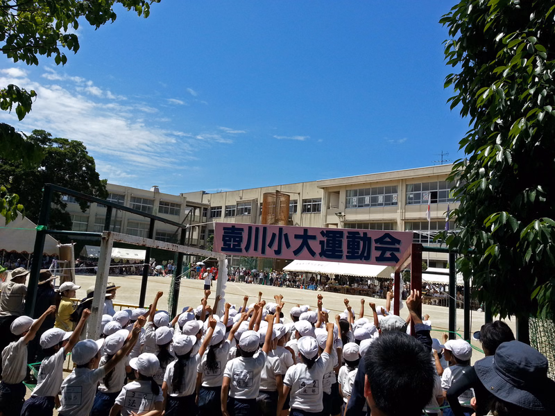 A large crowd gathers on a school field under a blue sky, with a banner reading "壹川小大運動會" visible.