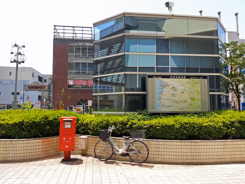 A modern glass office building features a large map display, with a red mailbox and bicycle parked in the foreground.