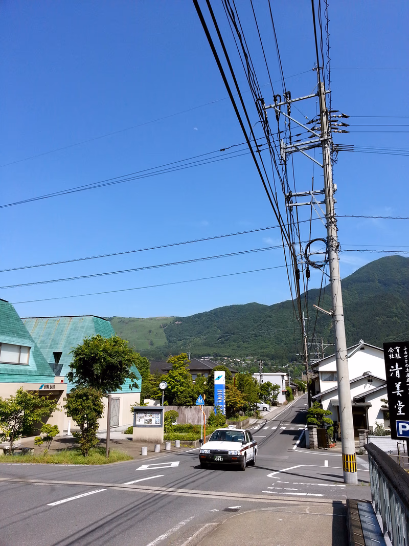 A car driving down a street in a small town surrounded by mountains and buildings.