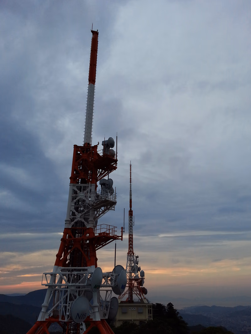 A photograph of a communication tower on a mountain at sunset.