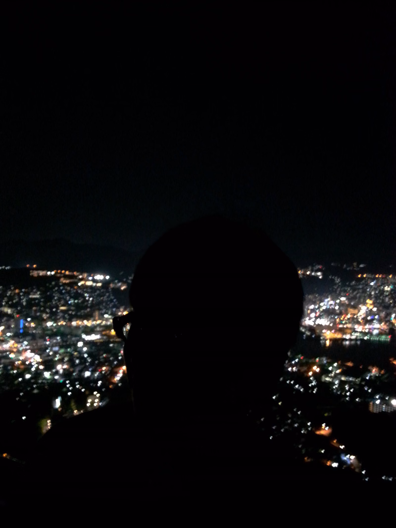 A silhouette of a person looking out over a brightly lit cityscape at night.