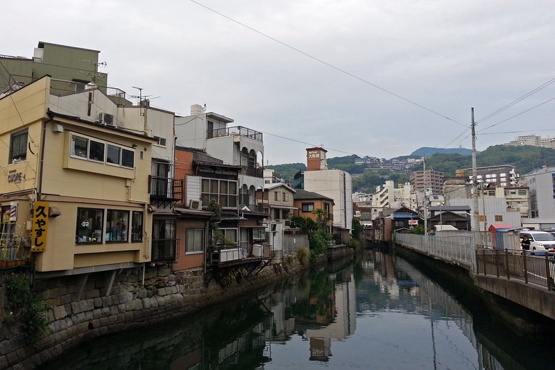 A view of houses lining a narrow canal in a city, with some signs visible, including one that reads "久やし".