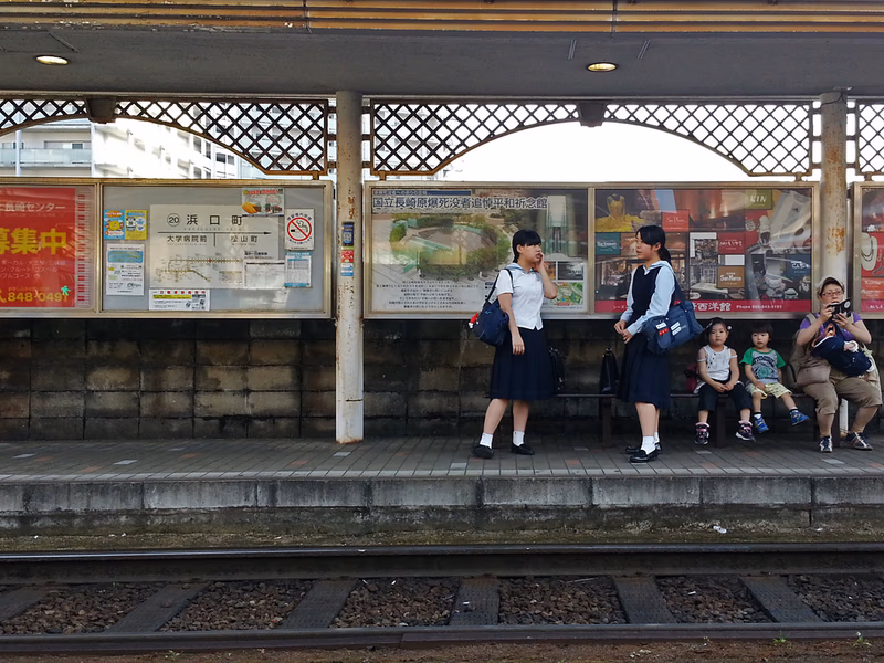 A school girl and a boy are waiting for the train at a train station.
