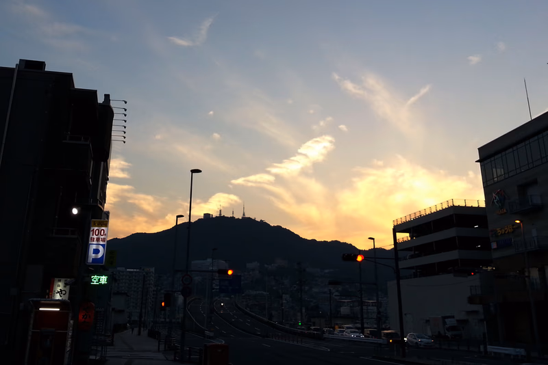 A photo of a city street at sunset with a mountain in the background.
