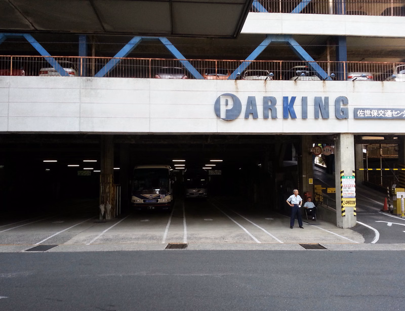 A concrete parking garage entrance with a large sign reading "PARKING" and Japanese text, with a bus visible inside.