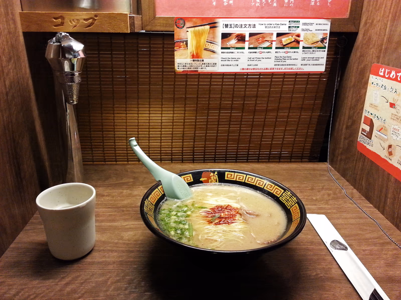 A bowl of ramen with a spoon, a cup, a menu, and a poster