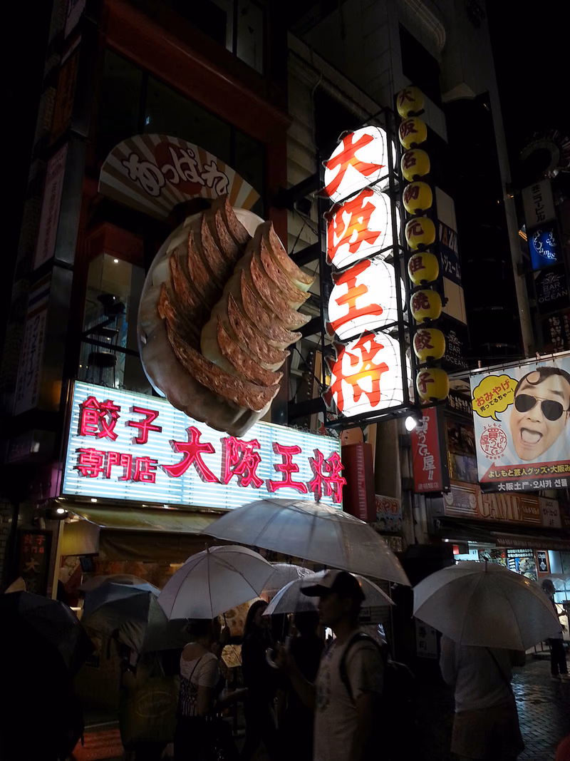 A night in the rain in Osaka, Japan, with a giant ice cream sign and people with umbrellas.