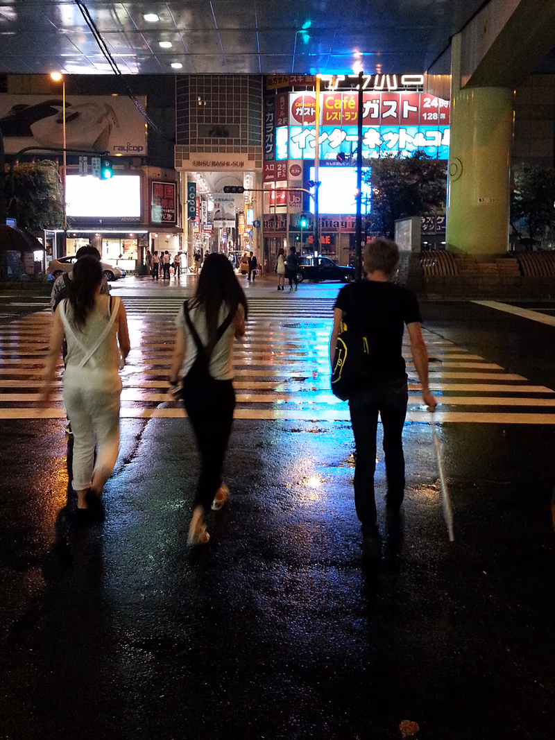 A night in the city, with people walking on a wet street.