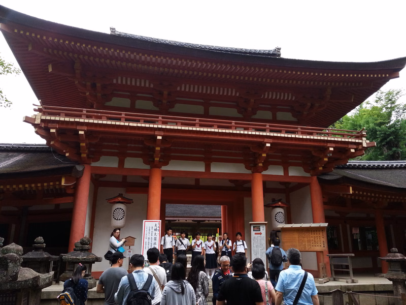 A large, traditional red wooden temple building with multiple tiers and a dark tiled roof stands in an outdoor setting.