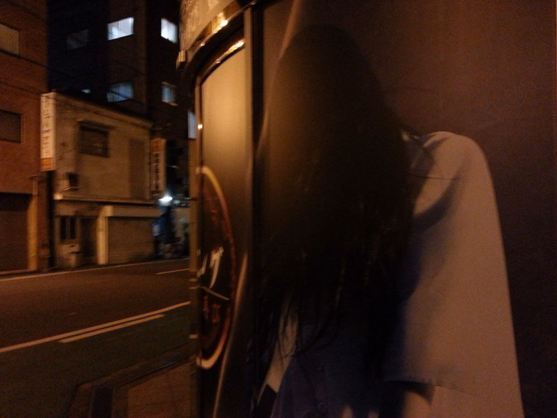 A person with long dark hair is visible near the window of a bus on a dark city street at night.