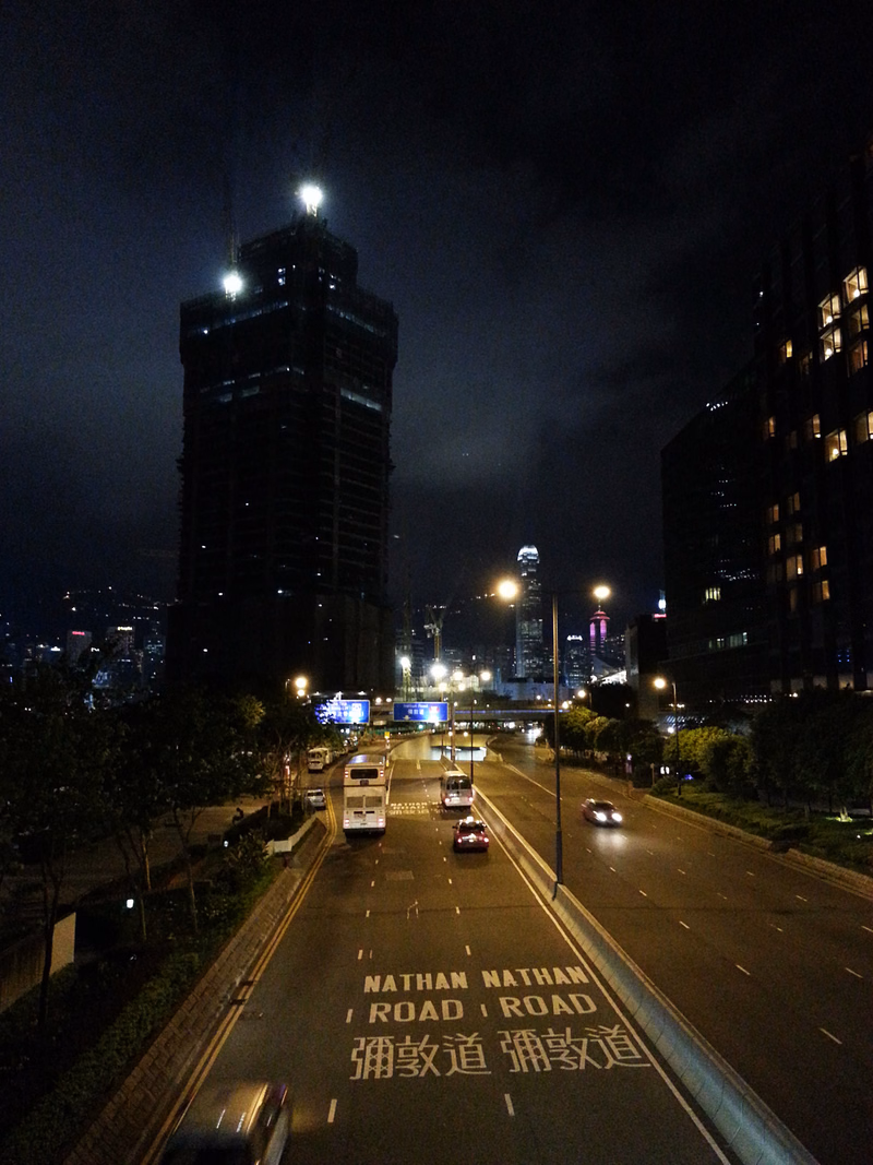 A nighttime cityscape view showing tall buildings and traffic on a road with a sign that reads "NATHAN NATHAN ROAD".