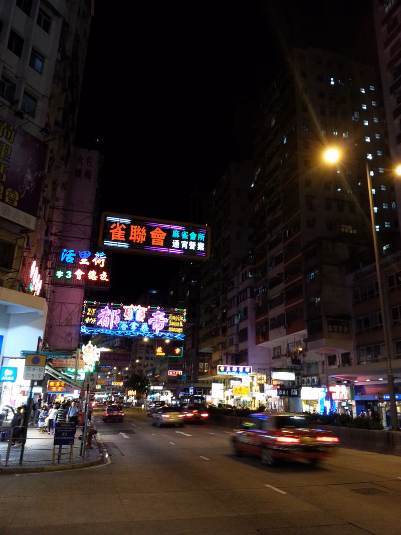 A nighttime view of a bustling city street in Kowloon City, Hong Kong.