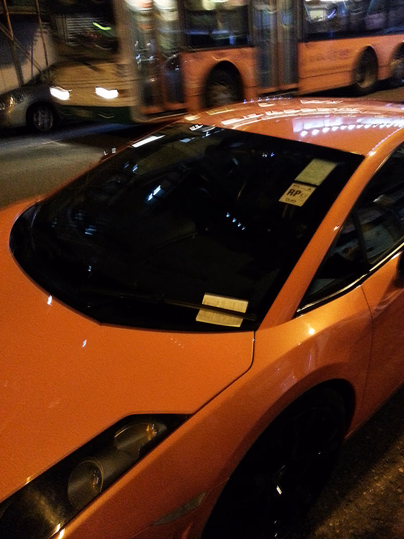 A bright orange car parked on a street at night.