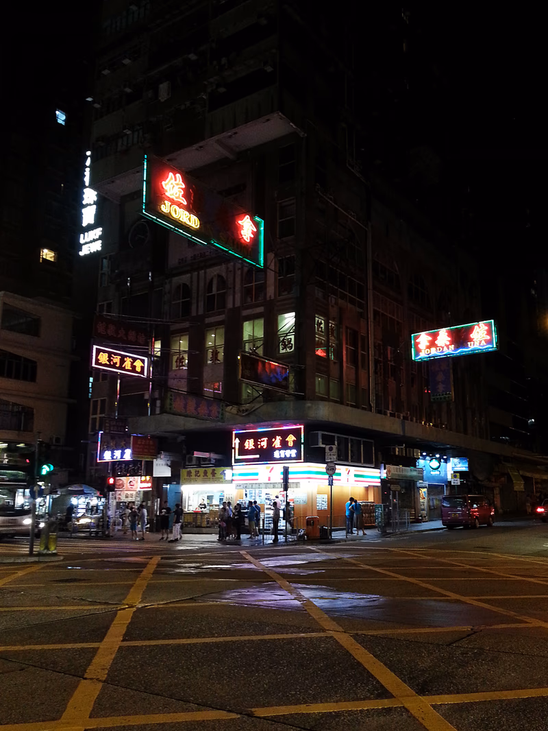 A nighttime view of a busy city street with illuminated signs and a few people walking by a bus.