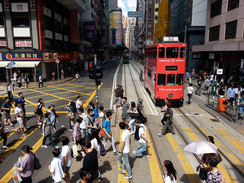 A bustling city street with a double-decker bus and a large crowd crossing the road.