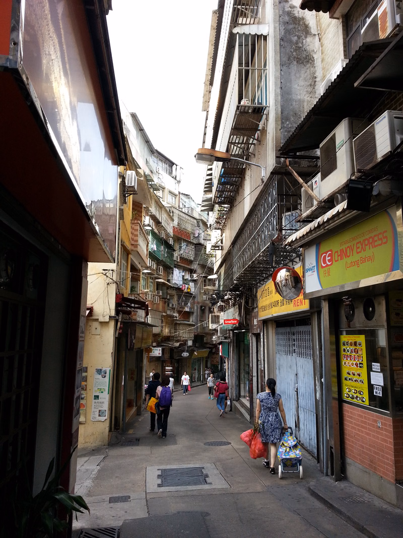 A narrow, crowded street lined with old shophouses, featuring a sign that reads "CE CHINOY EXPRESS (Lutong Bahay)".