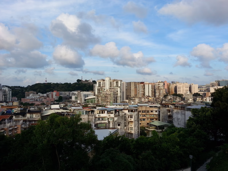 Aerial view of a city with a mix of old and new buildings, surrounded by greenery and a clear blue sky.