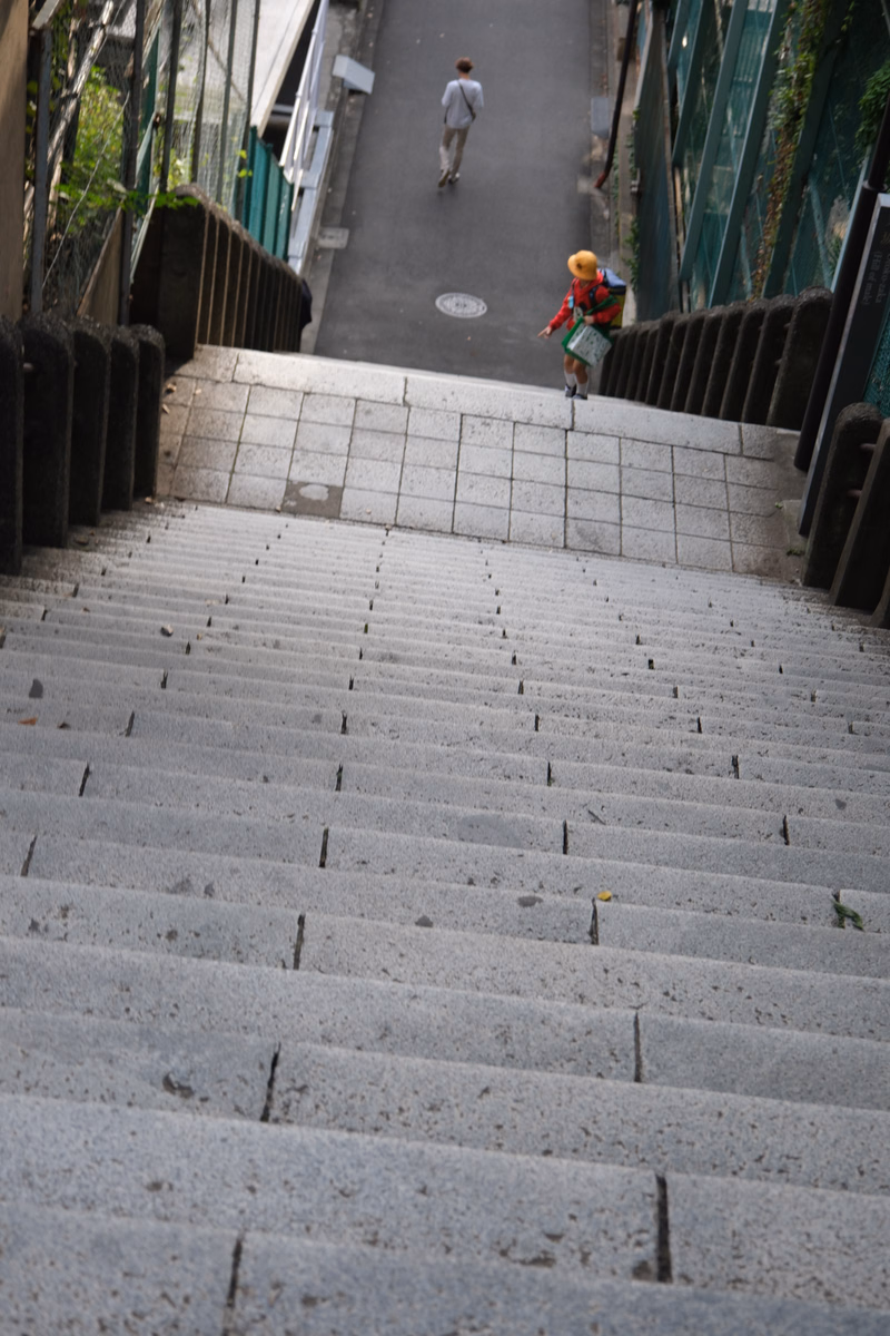 A person in a red and yellow jacket walks up a wide set of concrete stairs in an urban setting.