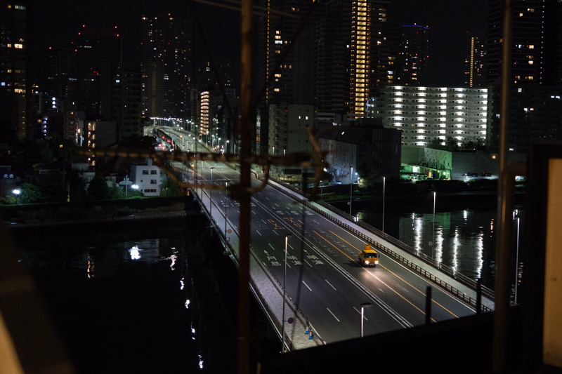 A nighttime view of a city skyline with tall buildings, featuring a bridge crossing over a dark river.