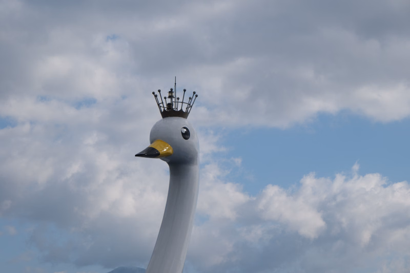 A white swan statue wearing a small crown is visible against a cloudy blue sky.