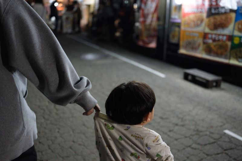 A child and an adult are walking together, and the adult is holding the child's shirt.