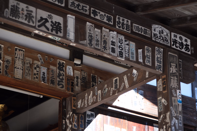A close-up view of a wooden facade covered with numerous vertical signs featuring Japanese text, including characters like "赤沢" and "久洋".