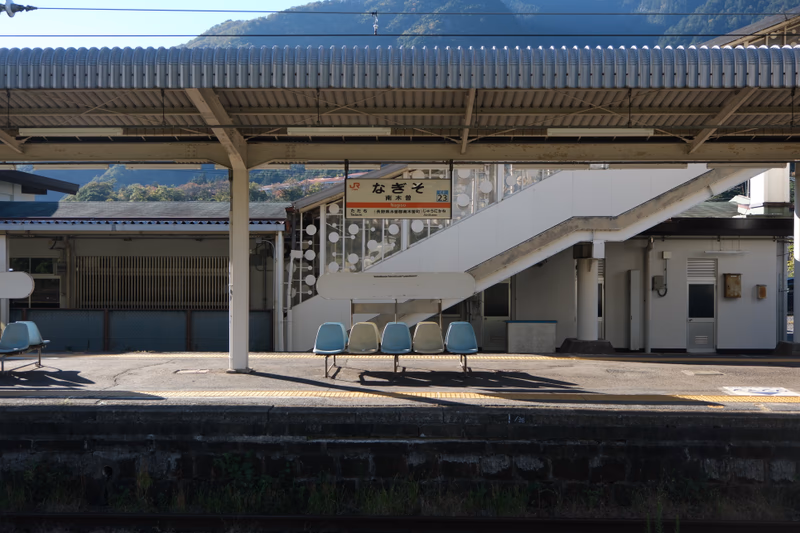 A quiet train station with a sign that reads 'Nagiso' and a mountain in the background.