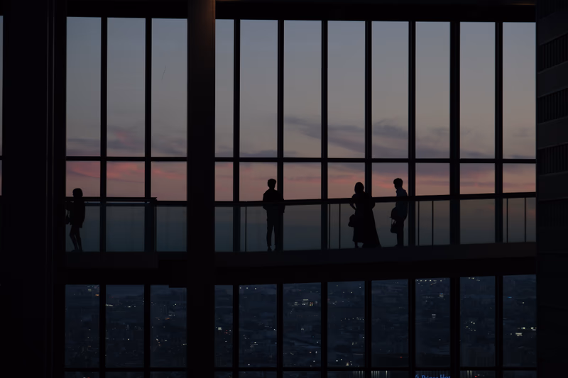 A photo of a cityscape at dusk with silhouetted figures on a glass floor.