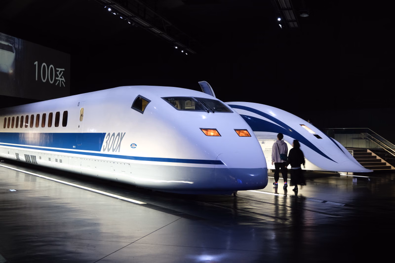 Two sleek, white bullet trains, one labeled "300X", are displayed indoors in a dark museum setting.