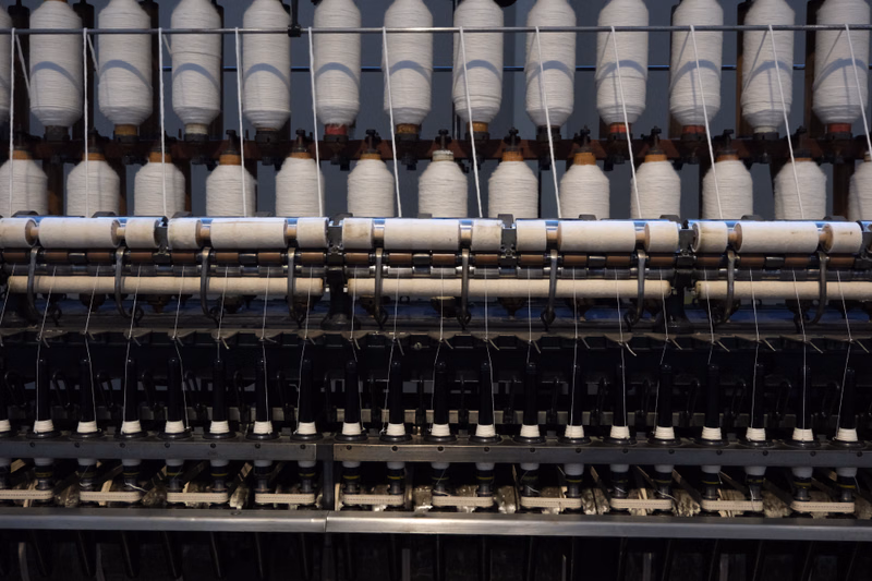 A close-up view of industrial spinning machinery with numerous spools of white yarn visible.