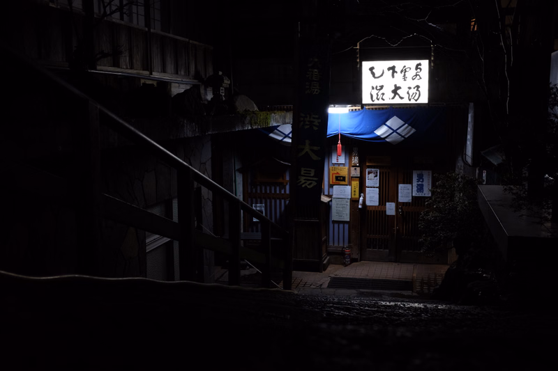 A Japanese temple entrance at night features a sign that reads "むし常 沢大坊" above the main gate.