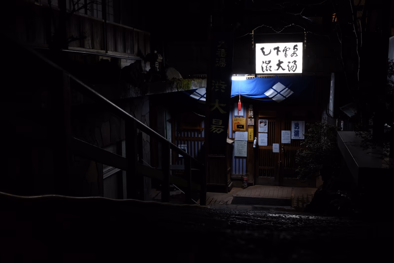 A nighttime view of a traditional Japanese restaurant with a modern sign and a staircase leading up to it.