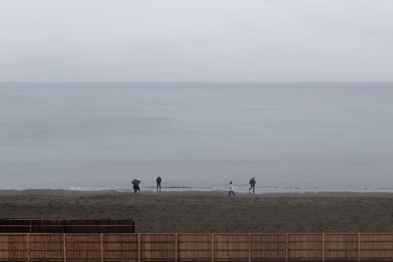 A photo of a beach with people walking near the shore and an overcast sky.