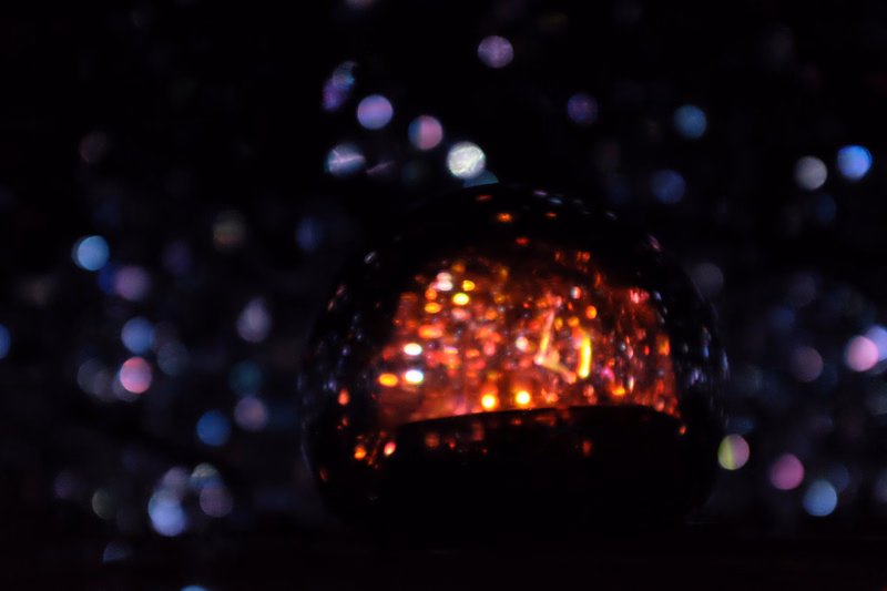 A dark, reflective sphere captures numerous bright, out-of-focus bokeh lights in the background.