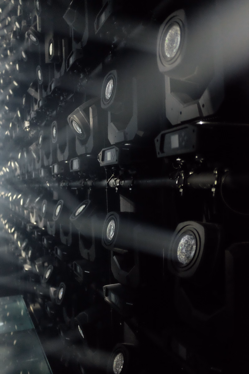 A row of powerful stage spotlights are aimed forward, creating bright beams of light in a dark setting.
