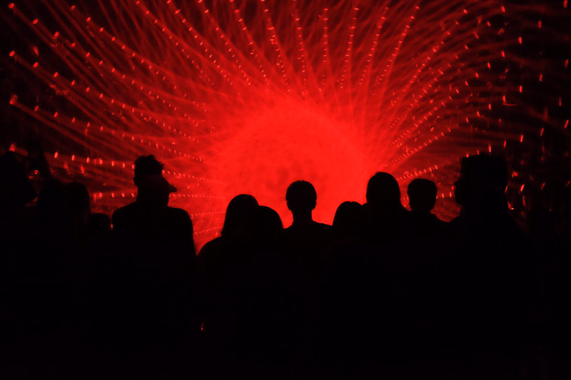 Silhouettes of a crowd watch a vibrant red light show during a concert.