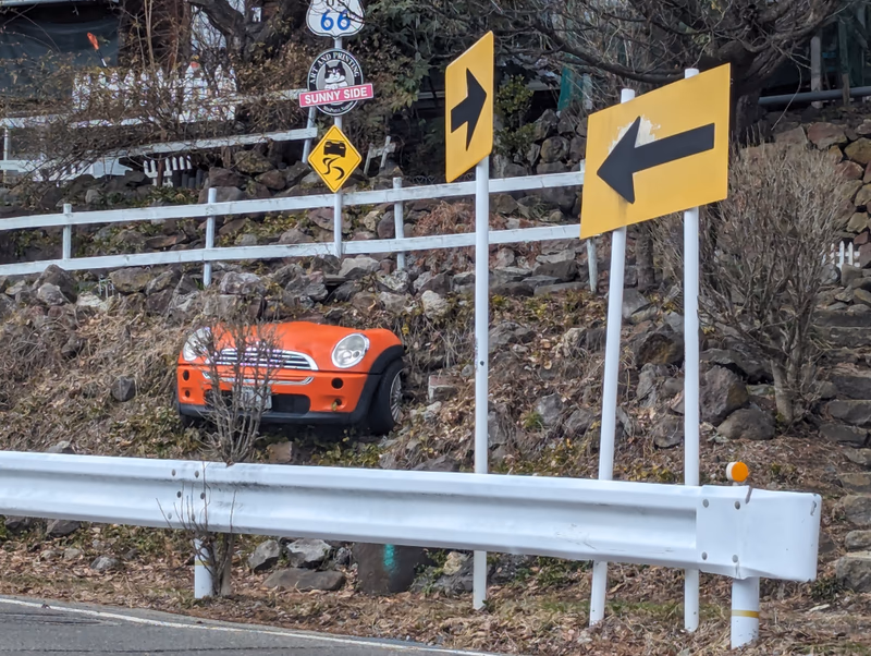 A car is placed on a hill, and there are road signs and a fence around it.