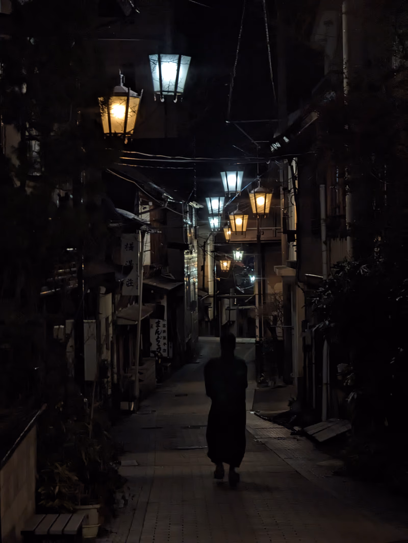A person walking alone in a narrow street lined with traditional Japanese lanterns at night.