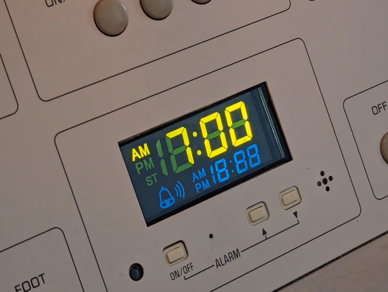 A close-up of a digital clock display showing the time as 12:00 AM and 6:08 PM.