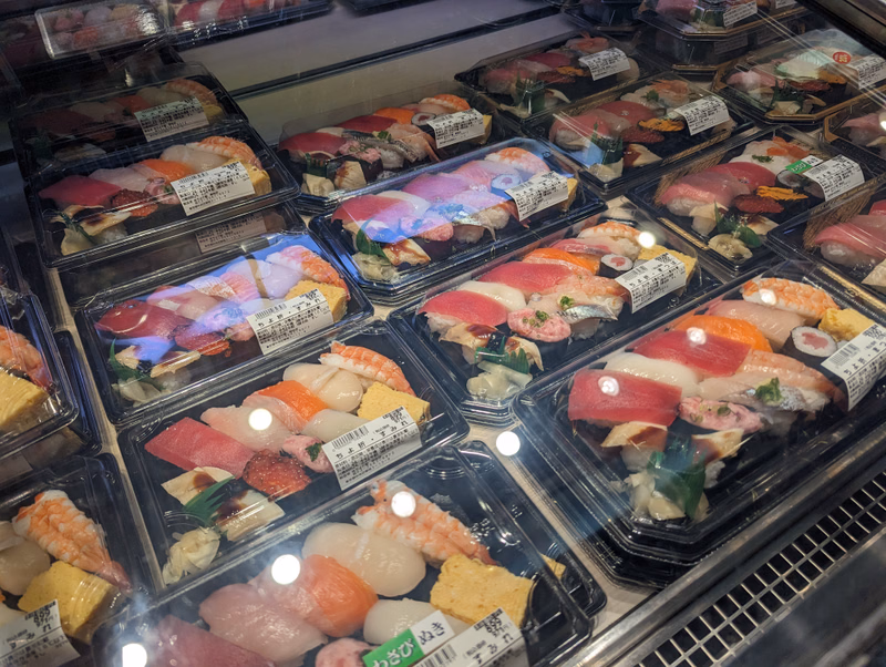 A refrigerated display case filled with various types of fresh sushi and sashimi, including rolls and slices of raw fish.