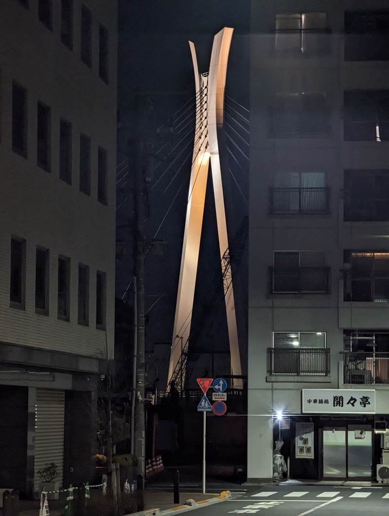 A large, modern, abstract metal sculpture stands in front of a glass-fronted building at night.