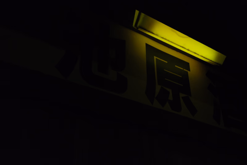 A photograph of a sign in a dark area with a bright yellow light illuminating it.
