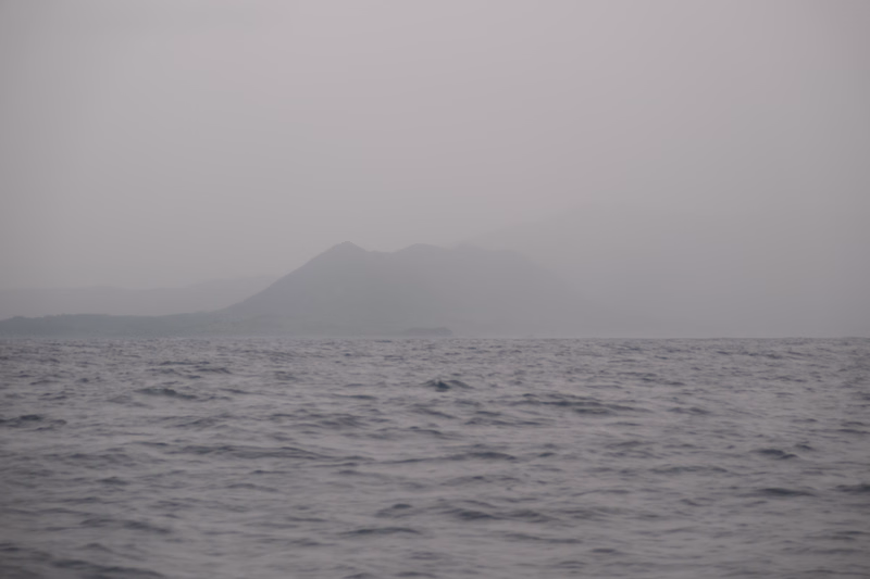 A hazy view of mountains rising from the ocean under a thick layer of fog.