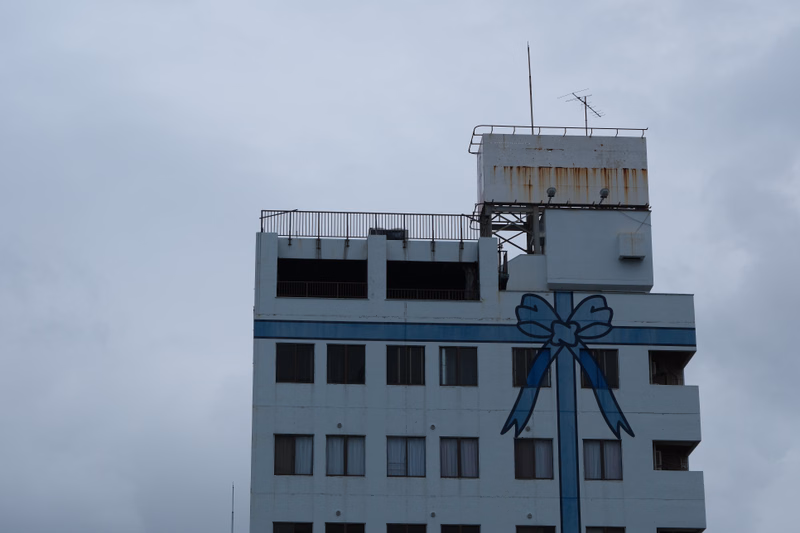 A multi-story building with a white facade and blue trim is visible against a cloudy, overcast sky.