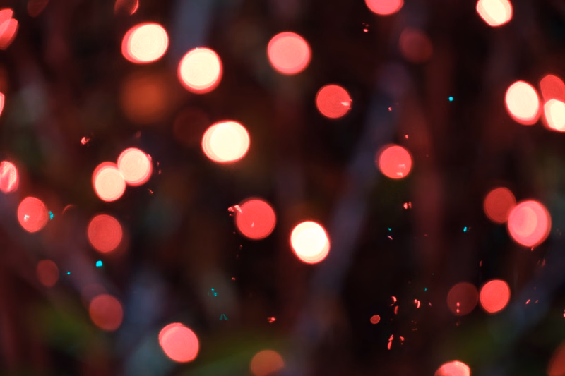 A close-up, blurred photograph of warm, glowing red and orange bokeh lights in an outdoor setting.