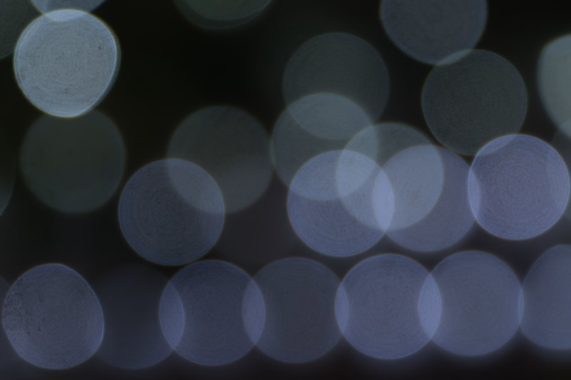 A close-up photograph of numerous circular, out-of-focus lights creating a bokeh effect against a dark background.